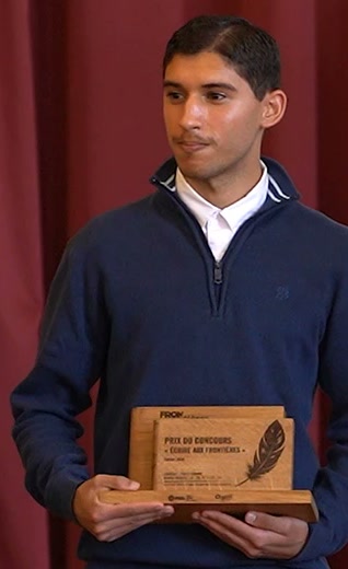 Portrait de Yanis Saouda, en pull bleu marine, tenant le trophée du concours Écrire aux frontières.