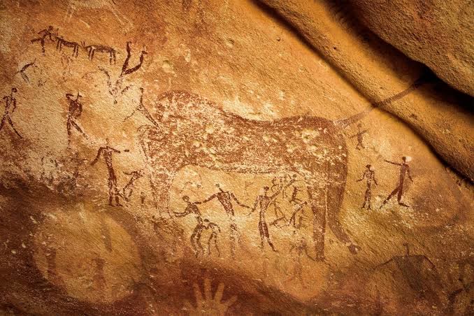 Peintures rupestres ocre : un grand animal entouré de silhouettes humaines.