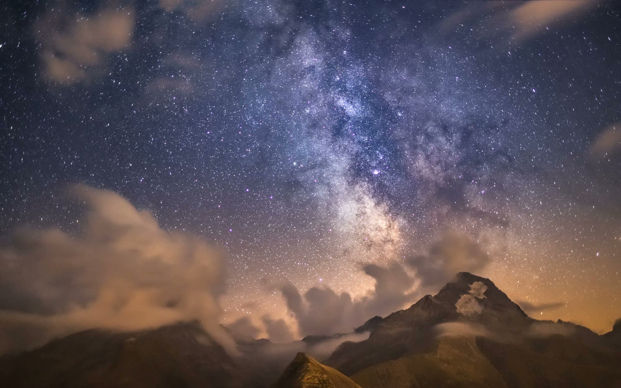 Un sommet sous la Voie lactée, entre nuages et étoiles.