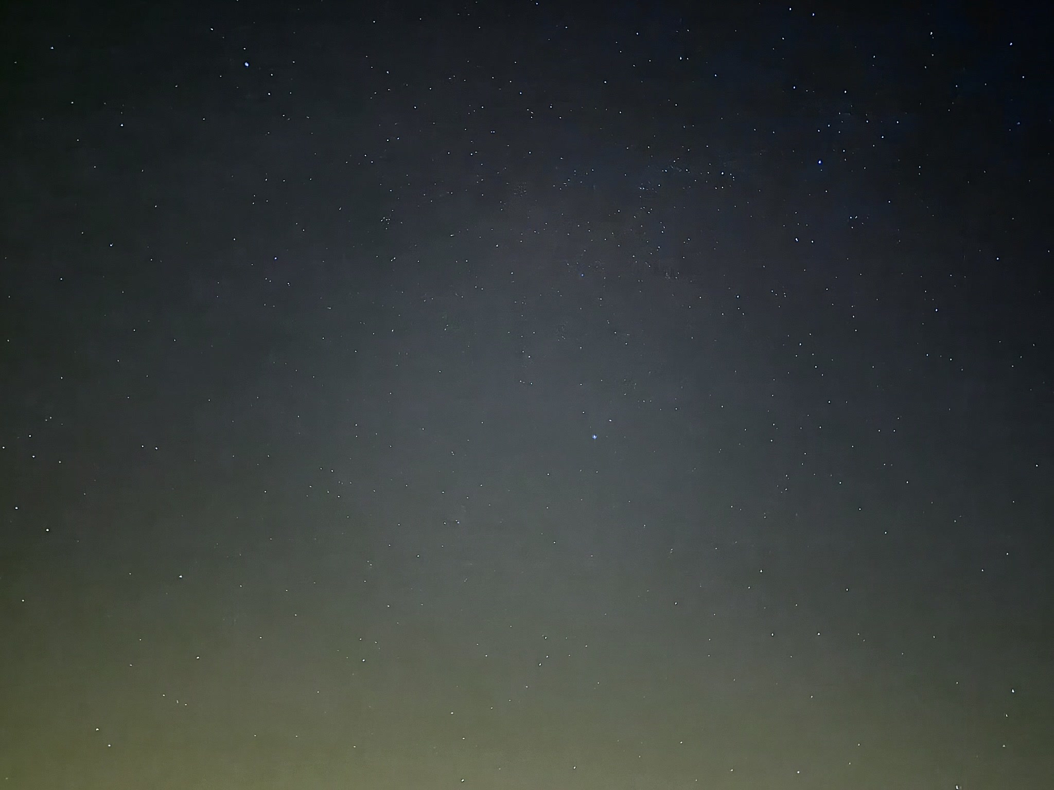 Un ciel étoilé au-dessus d'une lueur verte à l'horizon.