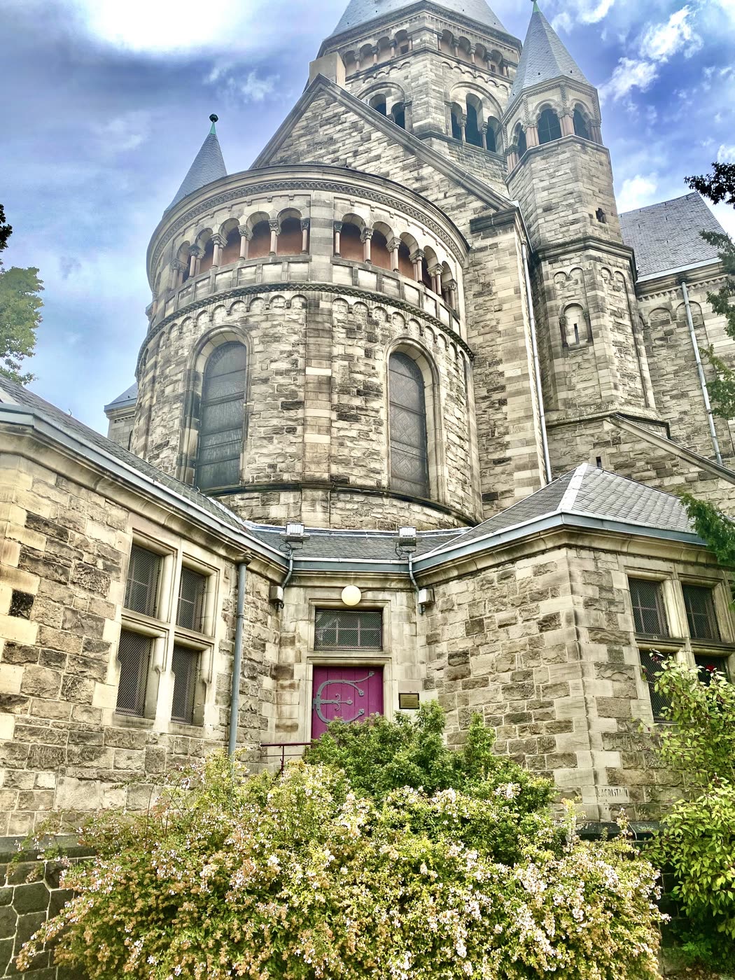 La façade d'une église de pierre en contre-plongée, au-dessus de massifs fleuris.