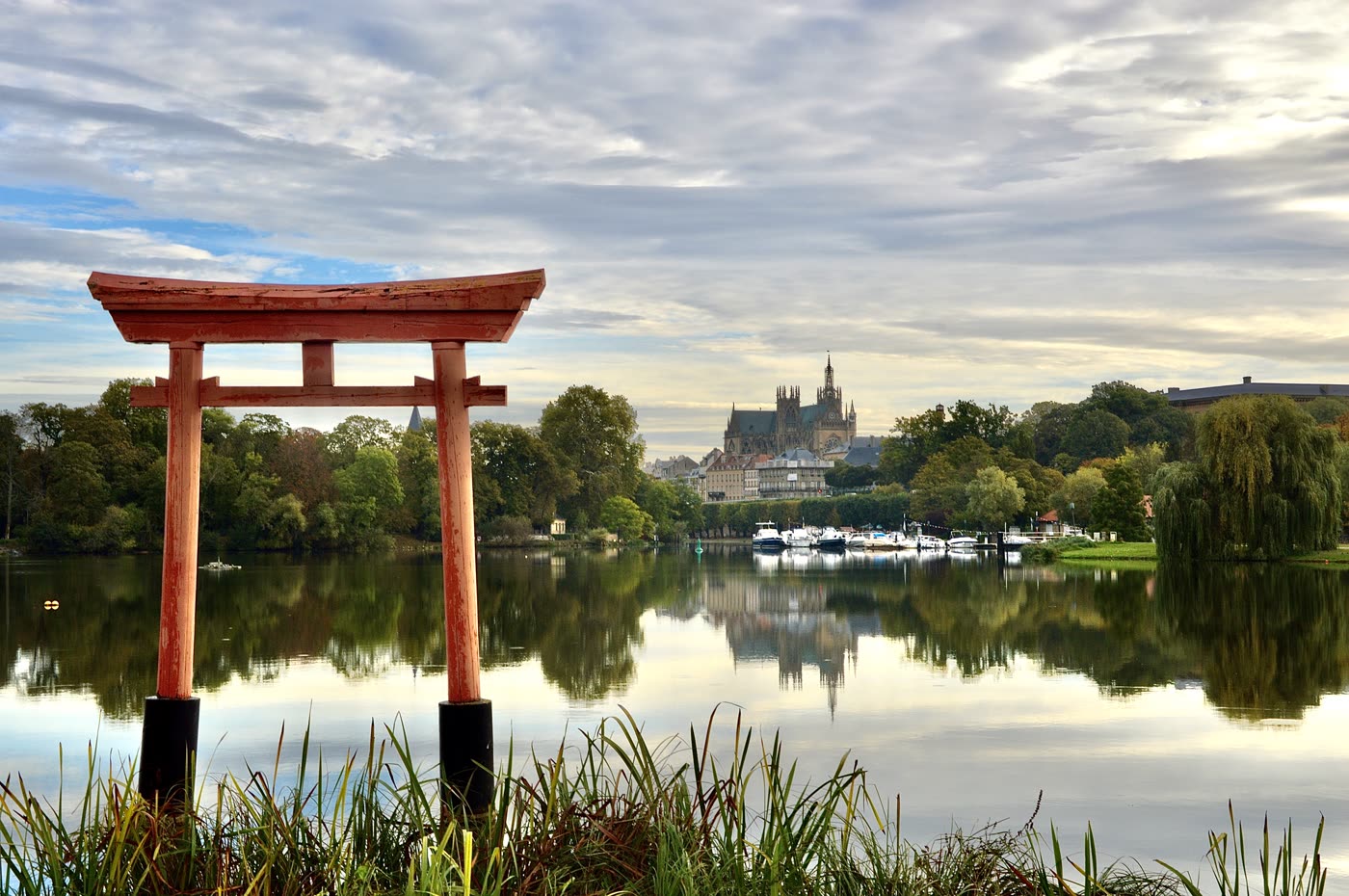 Un portique rouge de style japonais au bord d'un plan d'eau, la ville au loin.